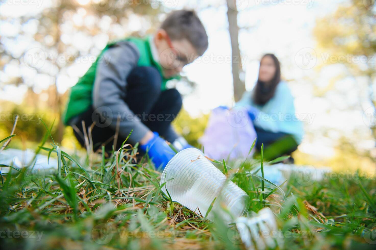 Smiling boy picking up trash in the park with his mother. Volunteer concept. photo