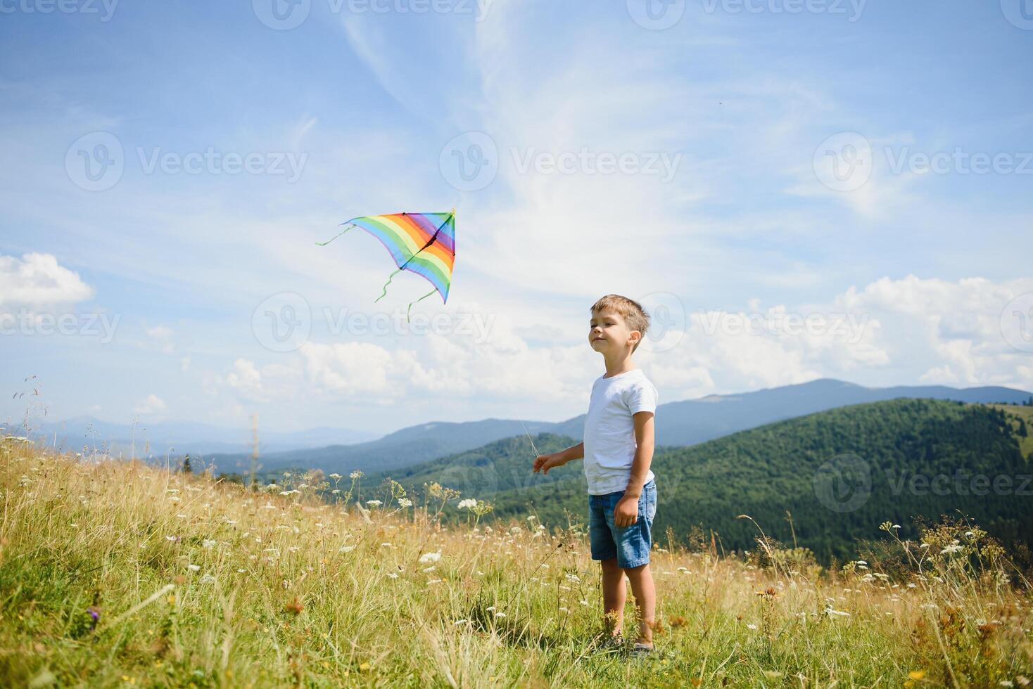 Little boy running on a background of mountains with kite. Sunny summer day. Happy childhood concept. photo