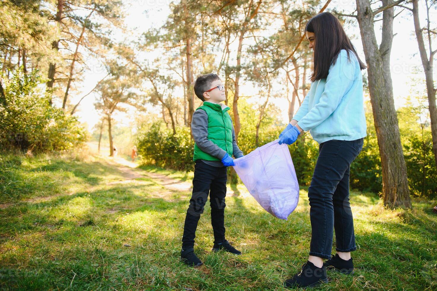 Smiling boy picking up trash in the park with his mother. Volunteer concept. photo