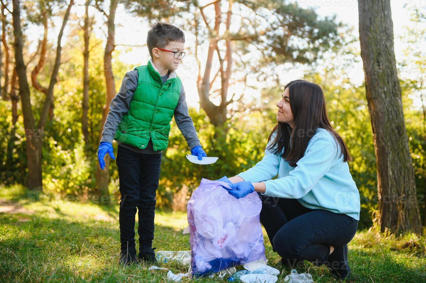 Mom teaches her son to clean up trash in nature. A woman removes plastic bottles in a bag. The topic of environmental pollution by garbage. photo