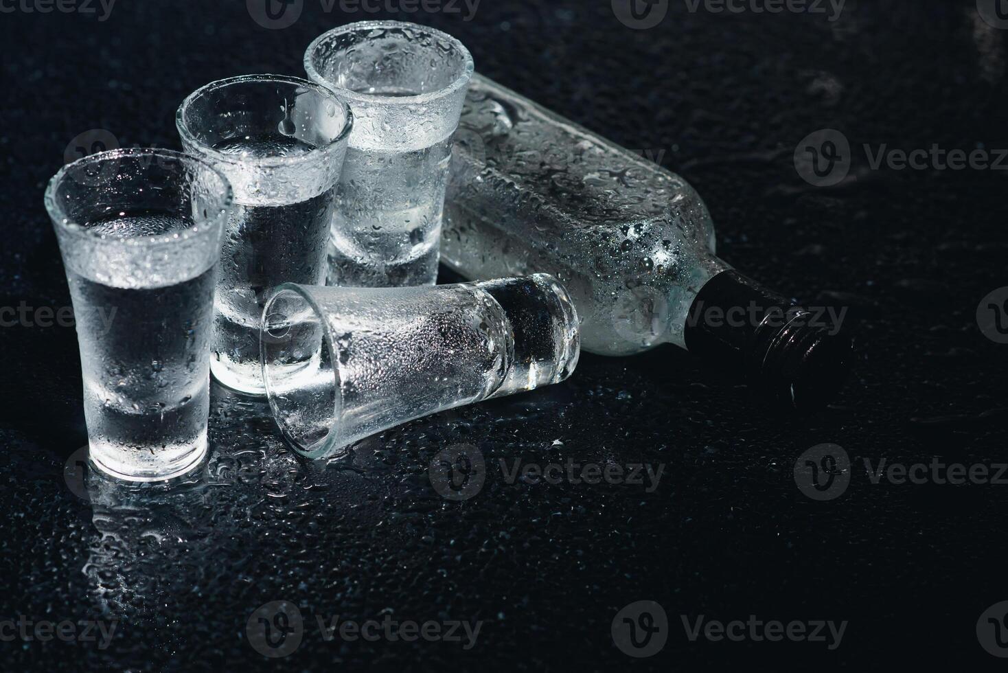 Close-up view of bottle of vodka with glasses standing on ice on black. photo