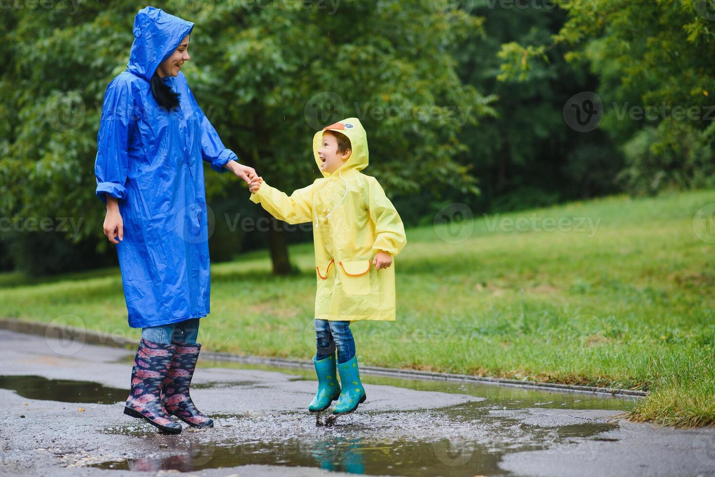 Mother with son walking in park in the rain wearing rubber boots photo