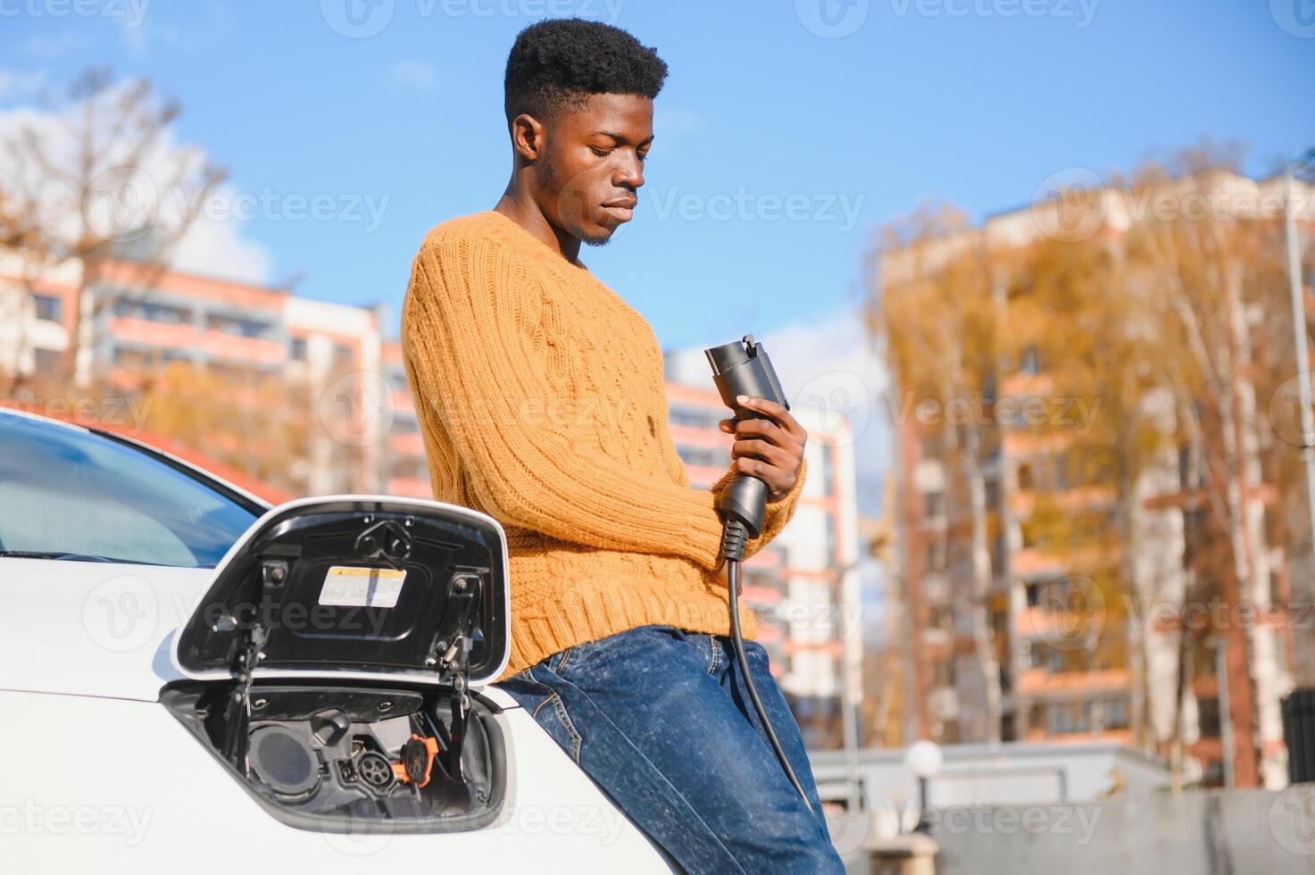 Electric cars, EV concept, eco friendly fuel. Portrait of young smiling black man, recharging his modern luxury electric car photo