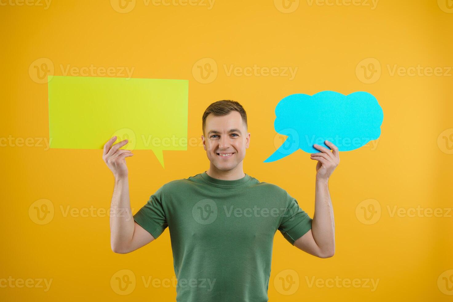 Portrait of cheerful smiling young handsome man holding and looking up at speech bubble with empty space for text on colorful yellow studio background photo