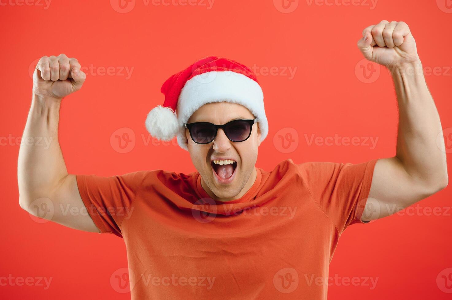 Portrait of happy and excited man in santa hat, rejoicing and winning something, celebrating new year, standing over red background photo