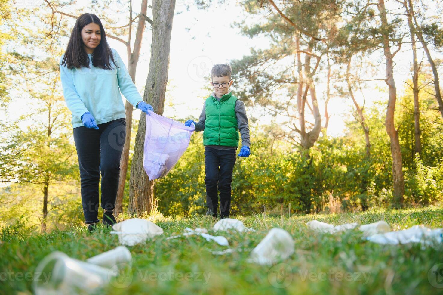 Smiling boy picking up trash in the park with his mother. Volunteer concept. photo