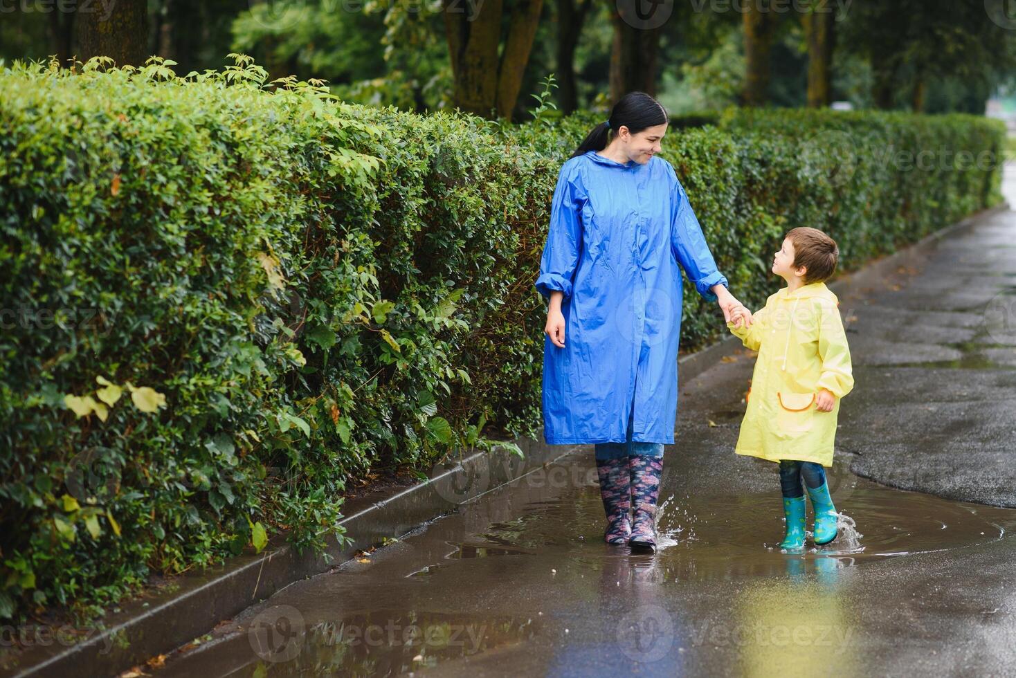 Mother and child, boy, playing in the rain, wearing boots and raincoats photo