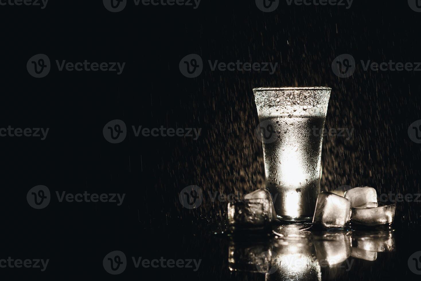 Vodka shot with ice on black table, copy space. photo