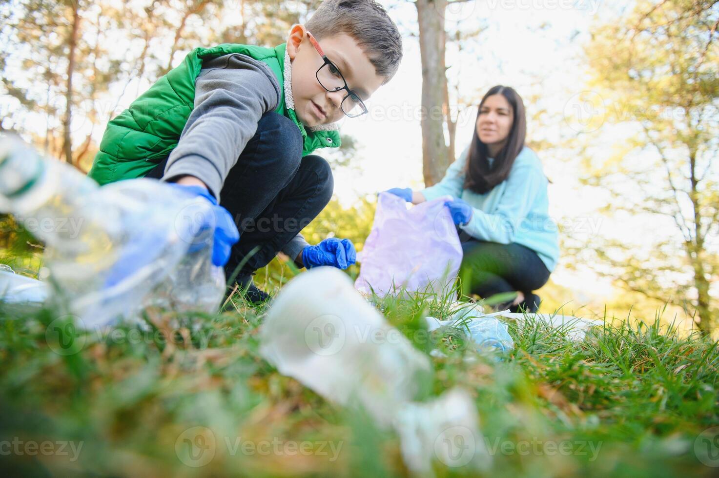 Smiling boy picking up trash in the park with his mother. Volunteer concept. photo