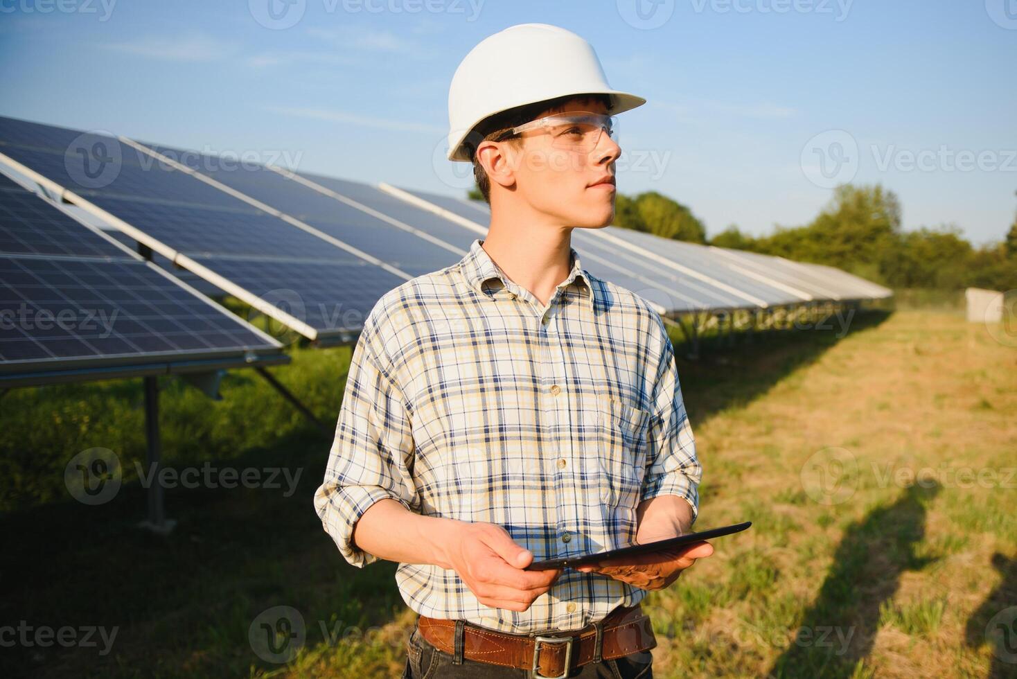 The portrait of a young engineer checks with tablet operation with sun, cleanliness on field of photovoltaic solar panels. Concept renewable energy, technology, electricity, service, green power. photo