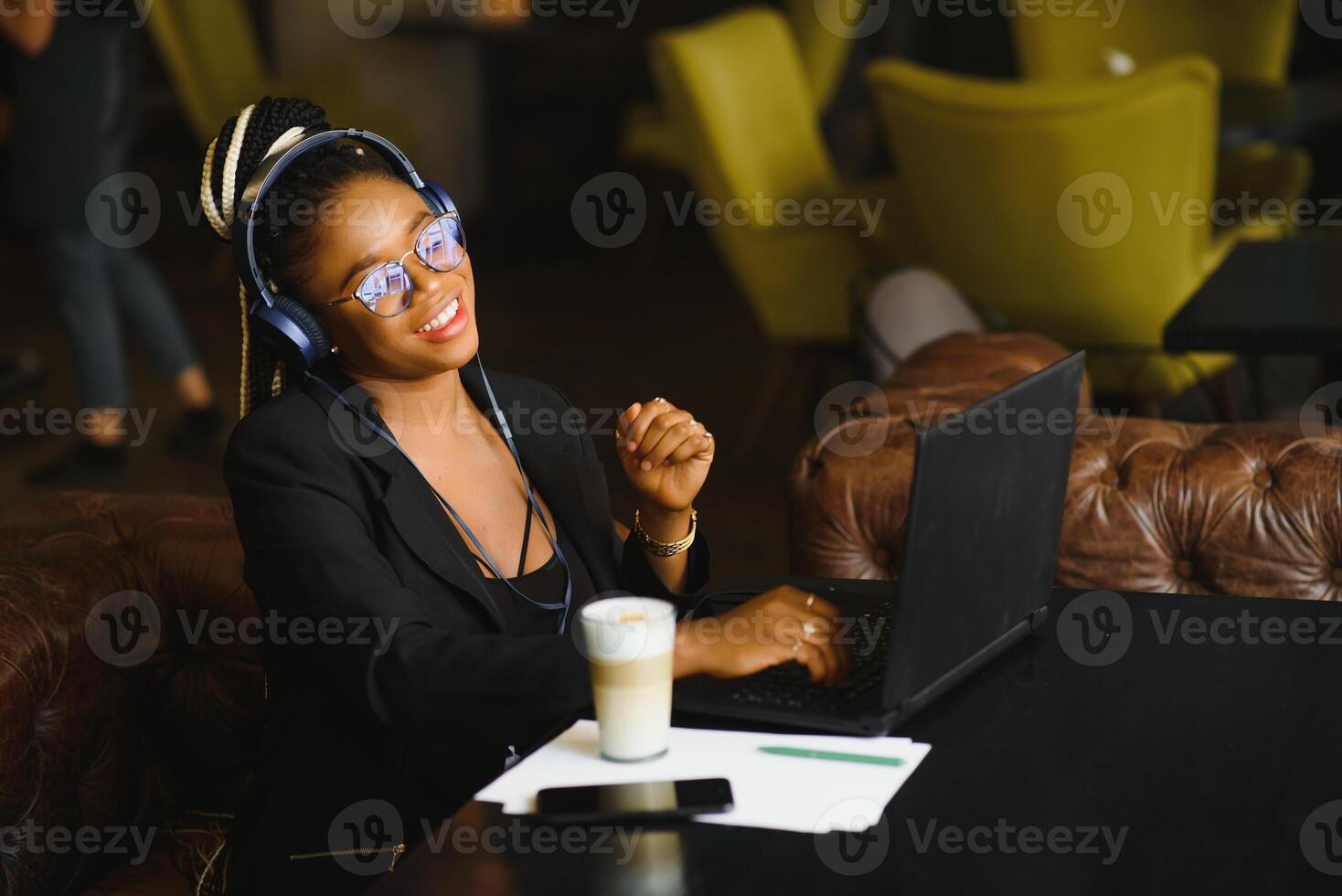 Attractive African American blogger with headphones and laptop communicating with followers in cafe photo