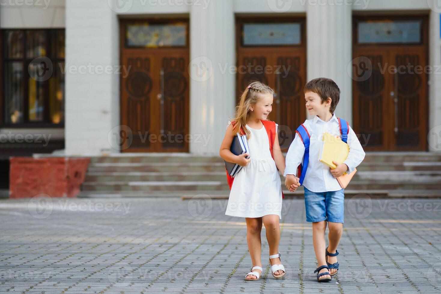 contento niños - chico y niña con libros y mochilas en el primero colegio día. emocionado a ser espalda a colegio después vacaciones. lleno longitud al aire libre retrato. foto