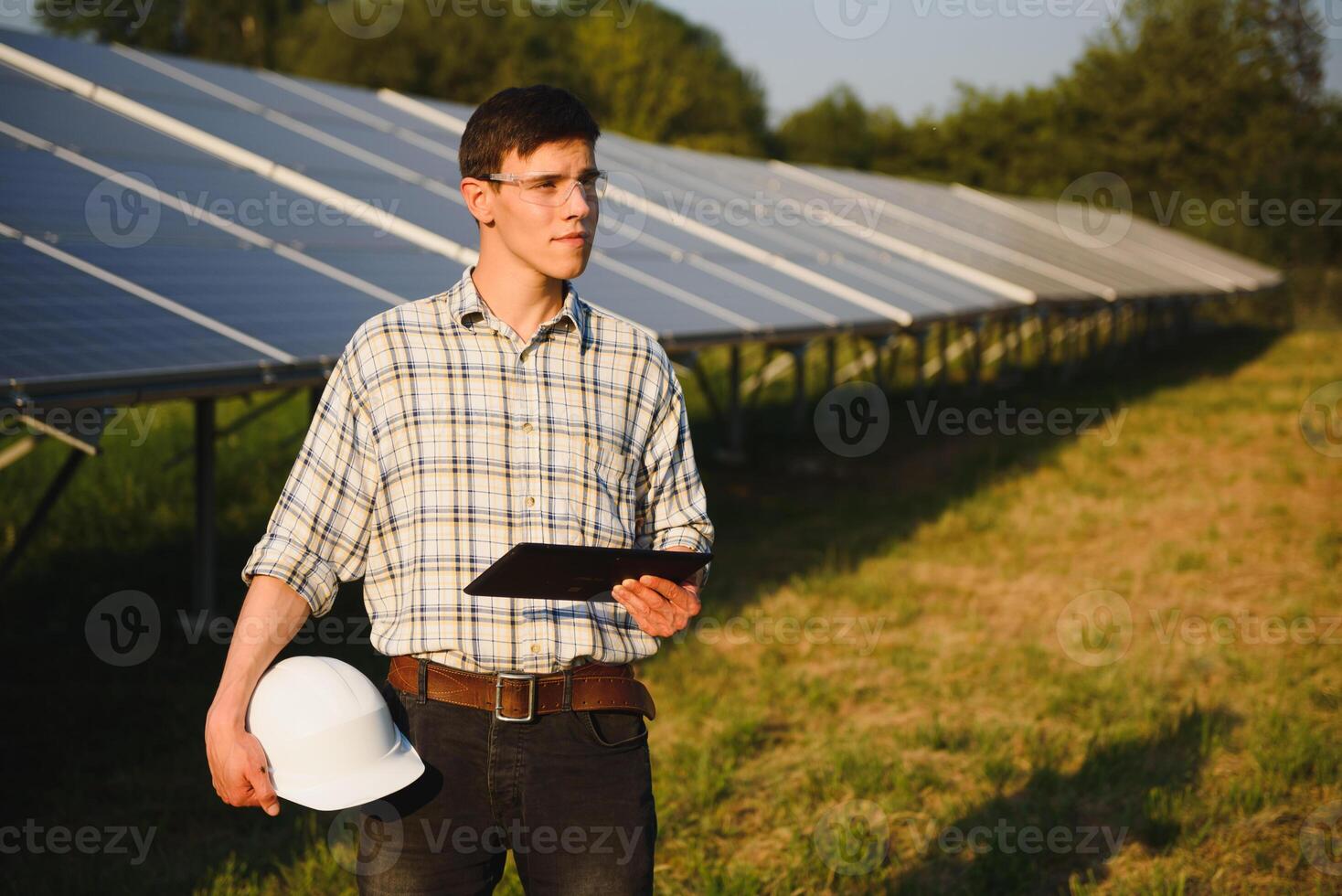 The portrait of a young engineer checks with tablet operation with sun, cleanliness on field of photovoltaic solar panels. Concept renewable energy, technology, electricity, service, green power. photo