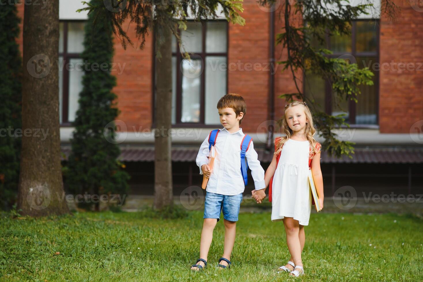 Happy children - boy and girl with books and backpacks on the first school day. Excited to be back to school after vacation. Full length outdoor portrait. photo