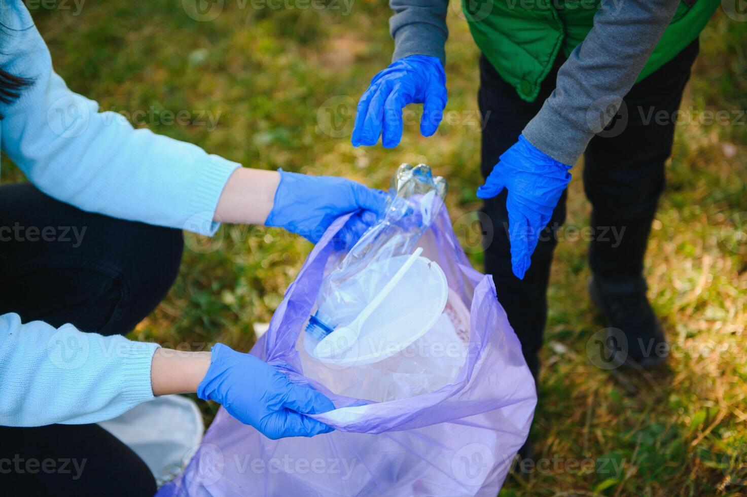 Smiling boy picking up trash in the park with his mother. Volunteer concept. photo
