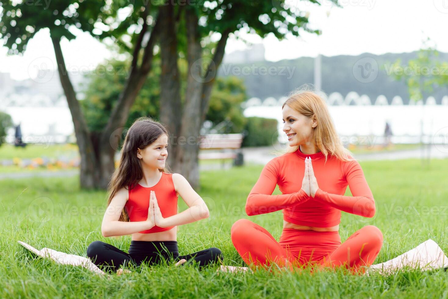 Mother and daughter doing yoga exercises on grass in the park at the day time photo