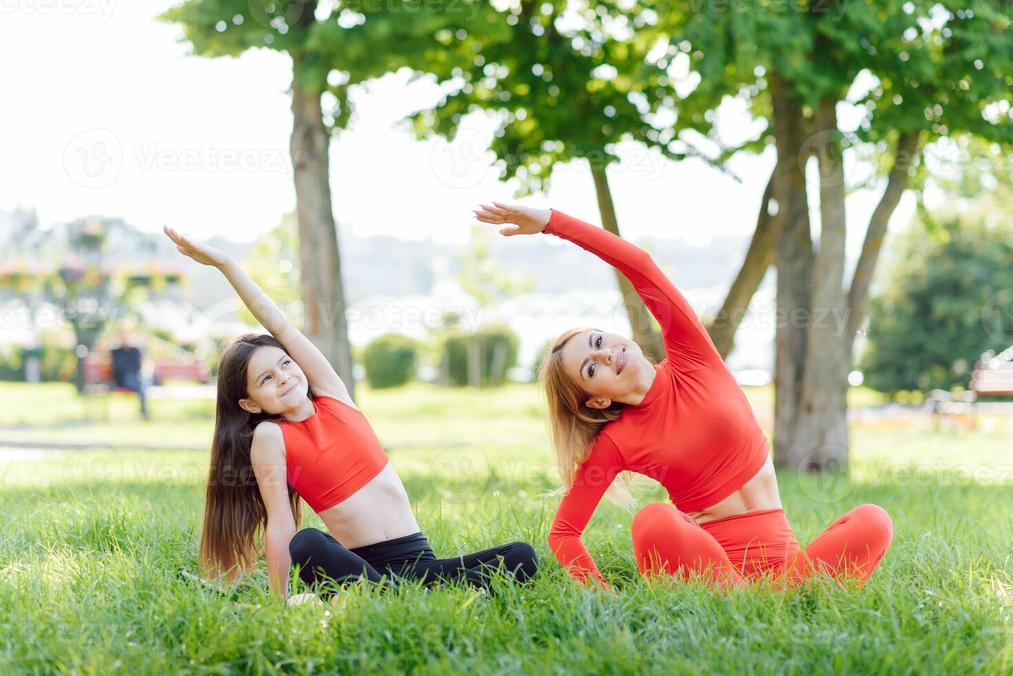 Mother and daughter doing yoga exercises on grass in the park at the day time. People having fun outdoors. Concept of friendly family and of summer vacation. photo