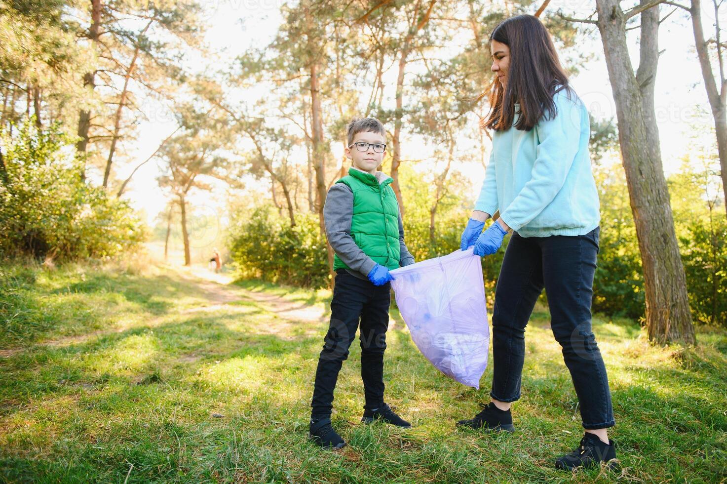 Smiling boy picking up trash in the park with his mother. Volunteer concept. photo