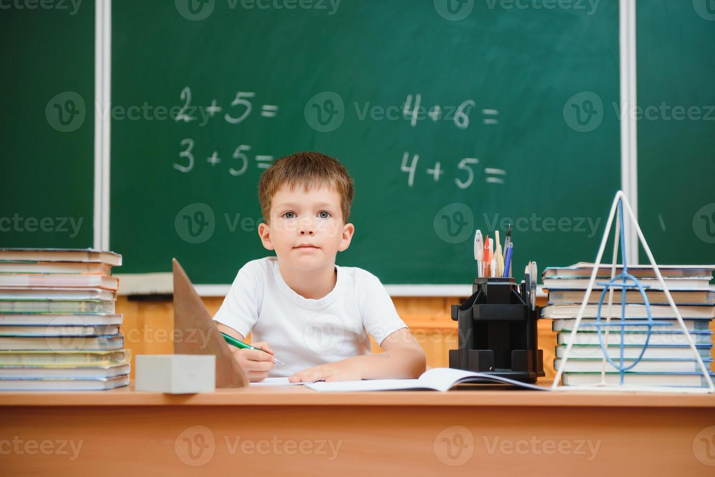 Back to school. Funny schoolboy sitting at a table with books in a school classroom. photo