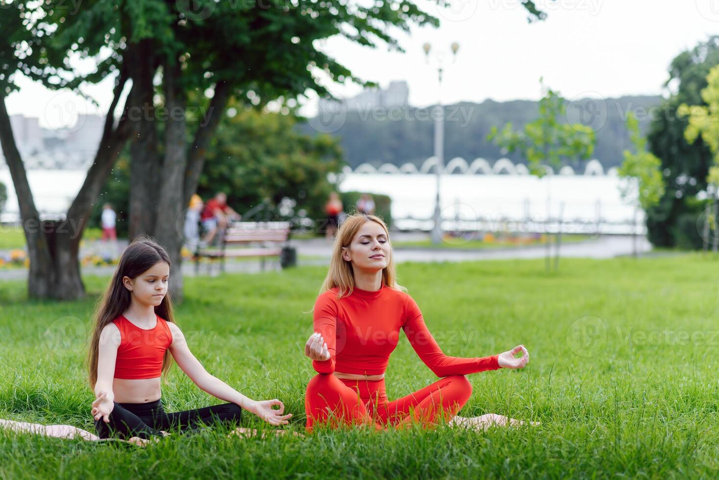 Mother and daughter doing yoga exercises on grass in the park at the day time photo