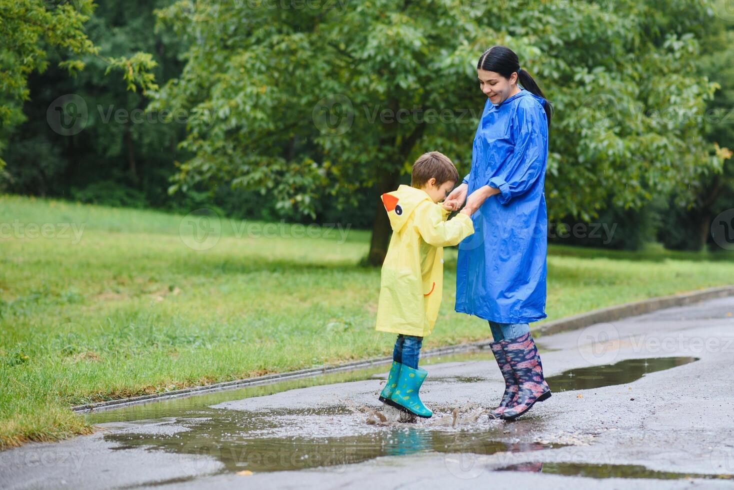 Mother with son walking in park in the rain wearing rubber boots photo