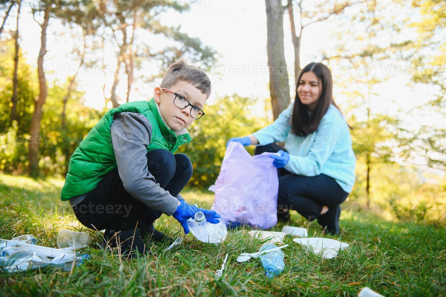 Mom teaches her son to clean up trash in nature. A woman removes plastic bottles in a bag. The topic of environmental pollution by garbage. photo