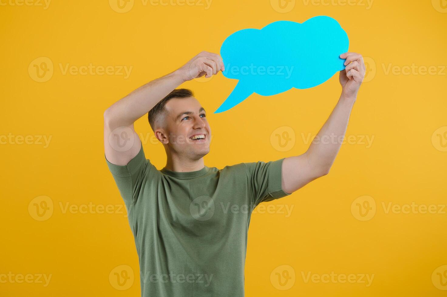 Cheerful young male pointing up and holding empty speech bubble with blank space for quote against vivid yellow background photo