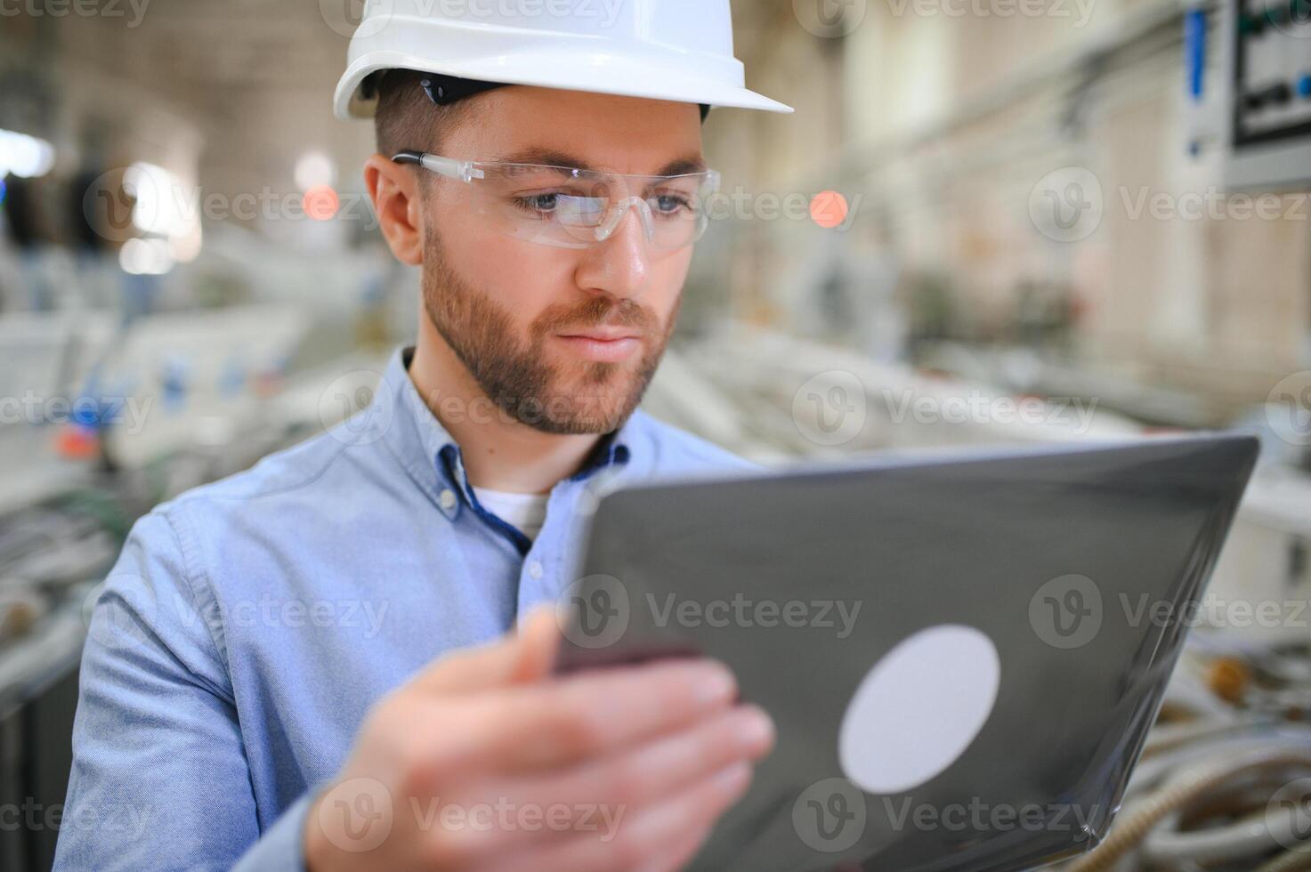 Engineer in hardhat is using a laptop in a heavy industry factory photo