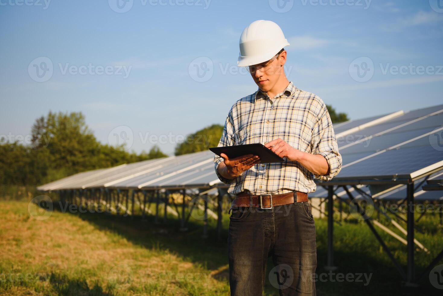 The portrait of a young engineer checks with tablet operation with sun, cleanliness on field of photovoltaic solar panels. Concept renewable energy, technology, electricity, service, green power. photo