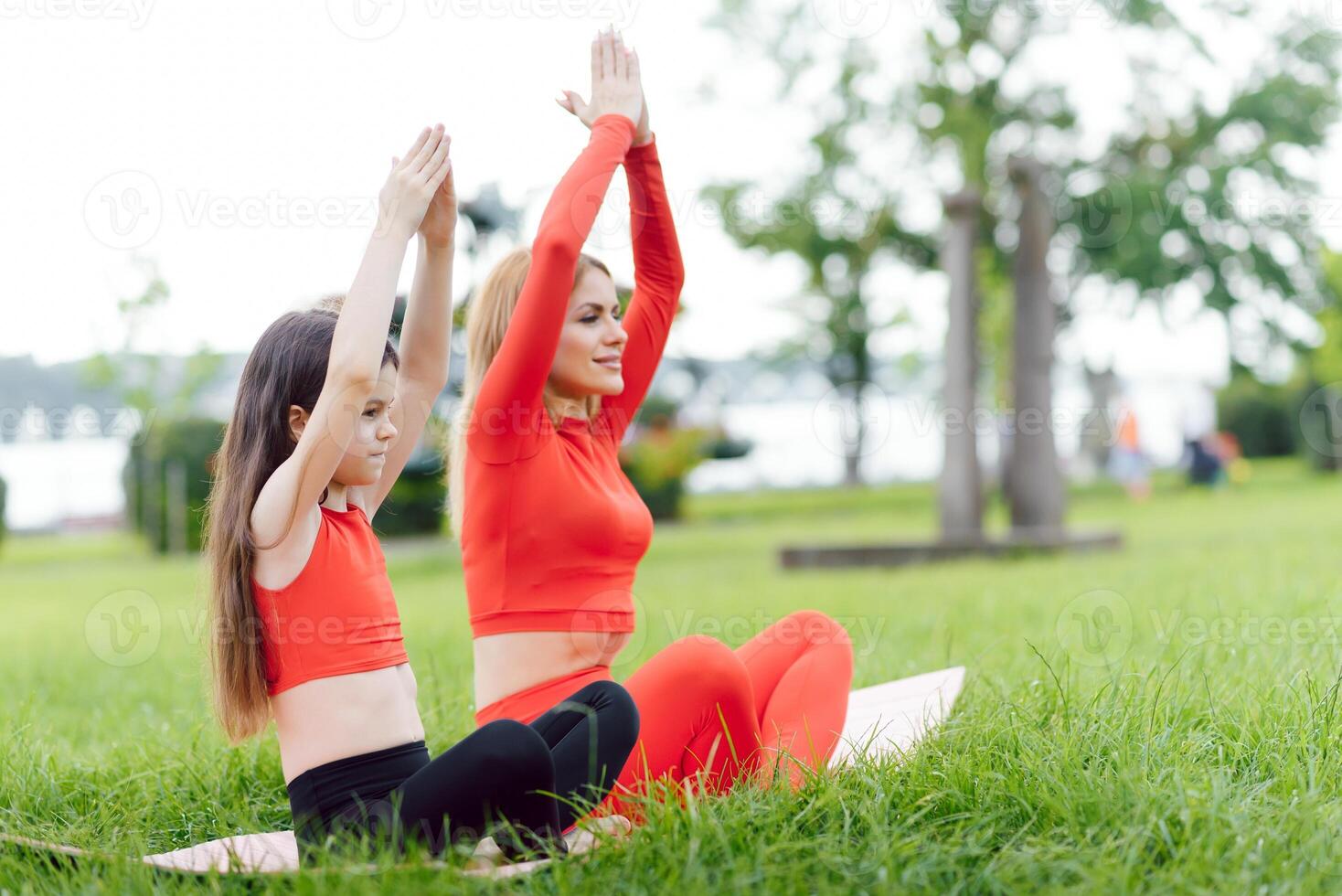 Mother and daughter doing yoga exercises on grass in the park at the day time photo