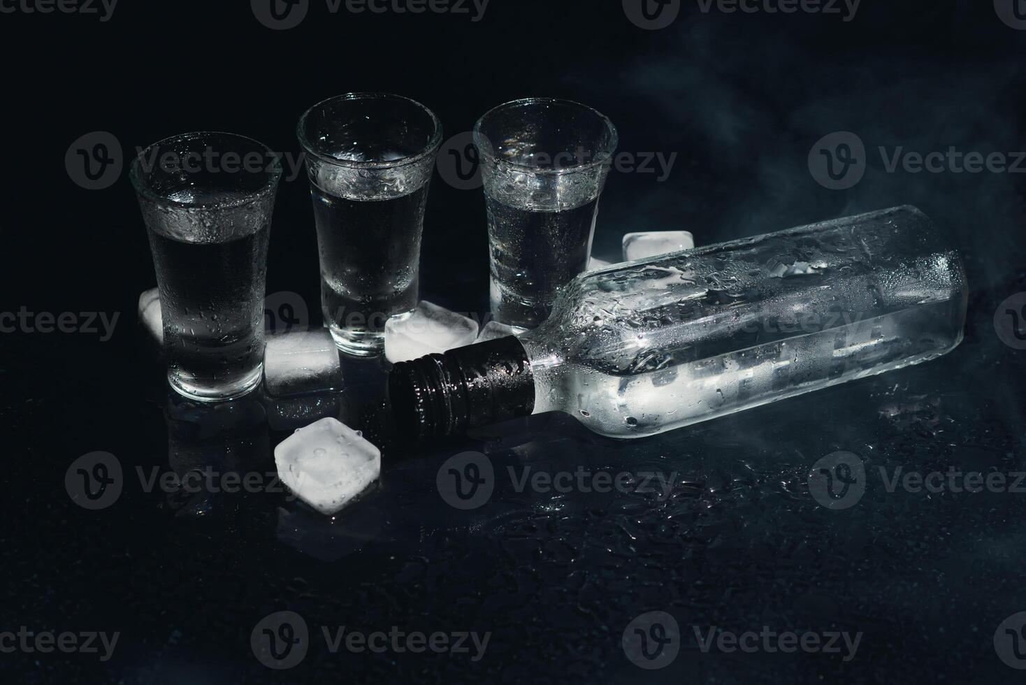 Close-up view of bottle of vodka with glasses standing on ice on black. photo