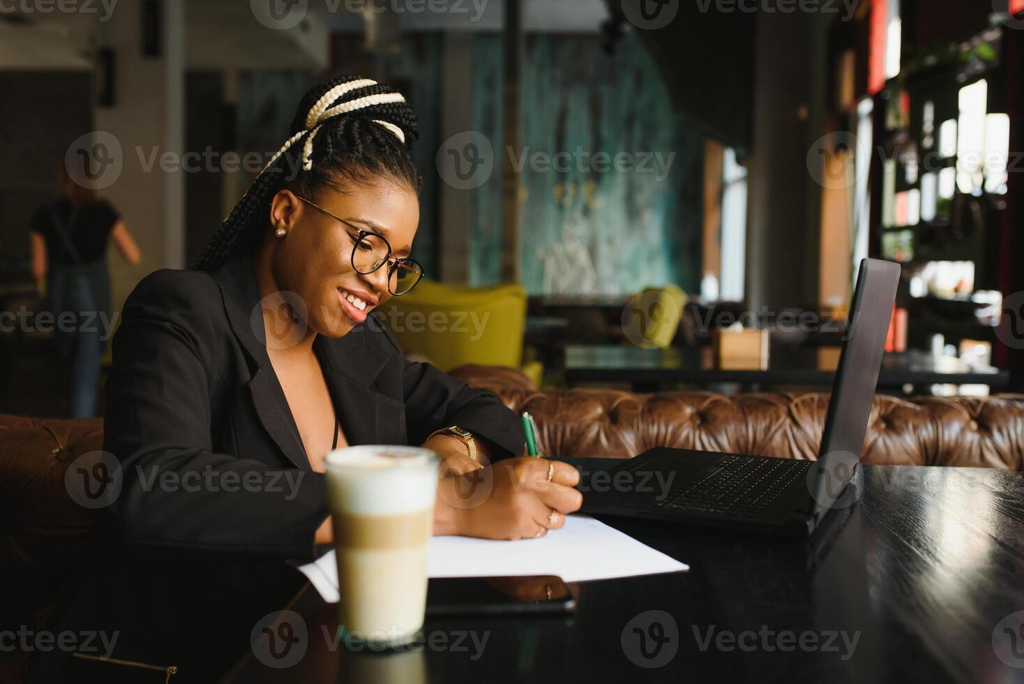 Student girl browsing Internet, using free wi-fi at cafe. African freelancer thinking on ideas for her blog, using laptop at co-working space, resting hand on wooden table, looking with inspired smile photo