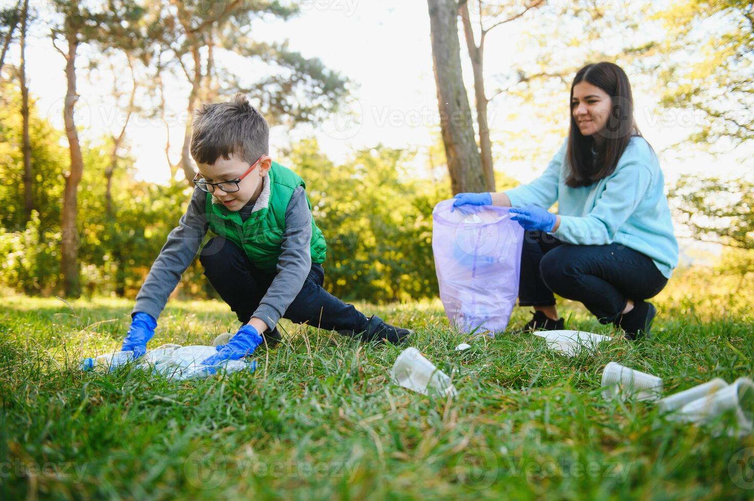 Smiling boy picking up trash in the park with his mother. Volunteer concept. photo