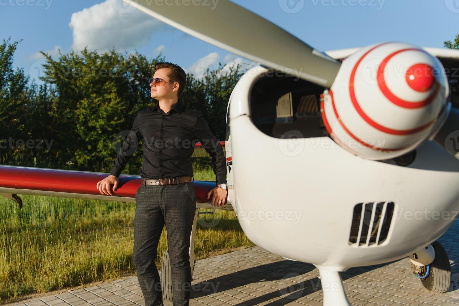 Young handsome businessman is standing near private plane. Confident and successful man in airport. photo