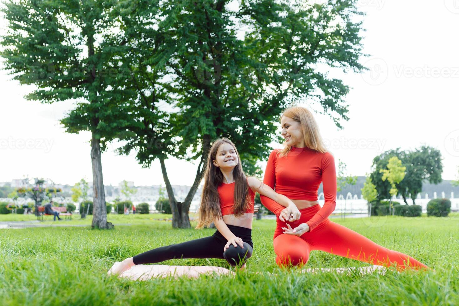 Mother and daughter doing yoga exercises on grass in the park at the day time. People having fun outdoors. Concept of friendly family and of summer vacation. photo