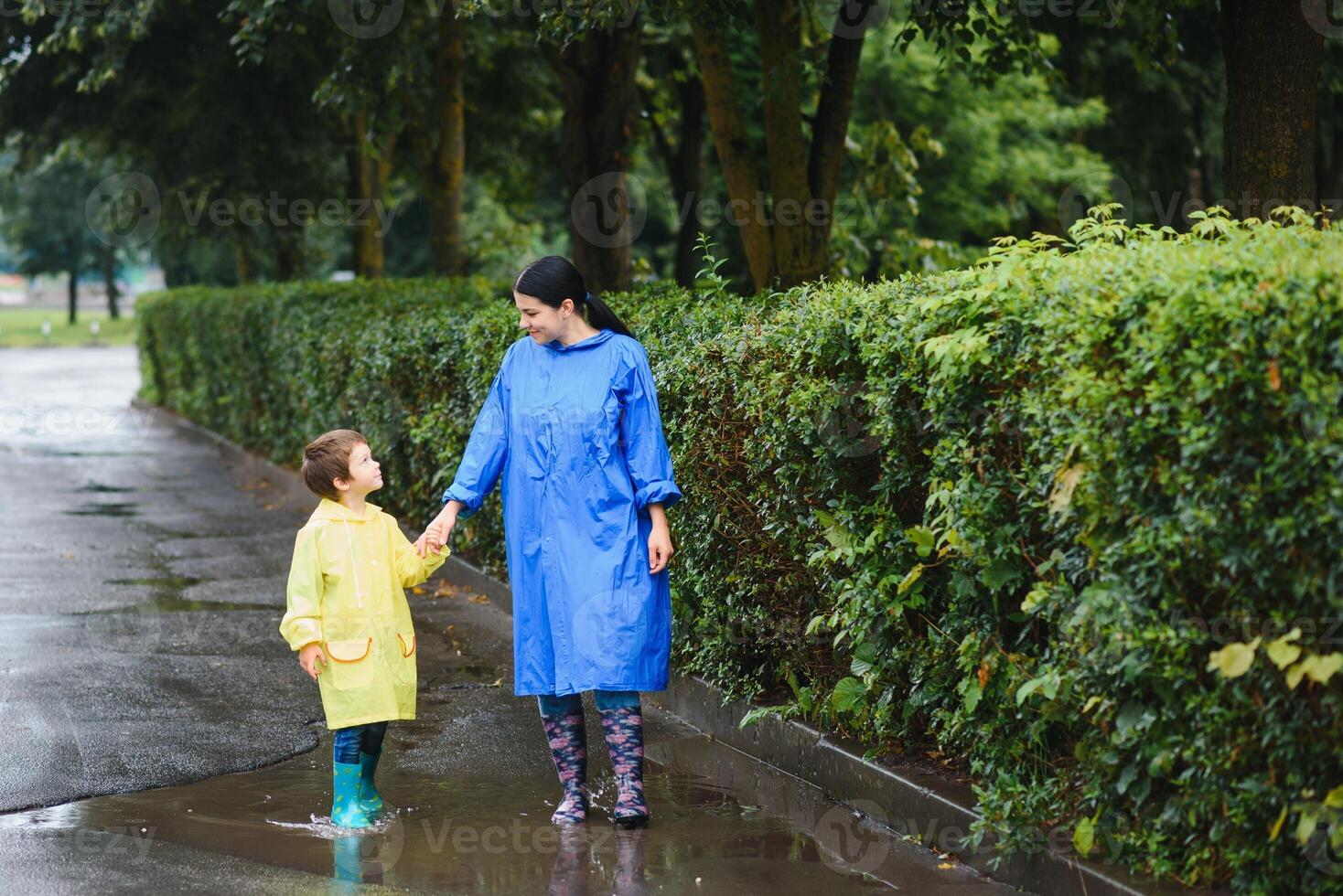 Mother with son walking in park in the rain wearing rubber boots photo