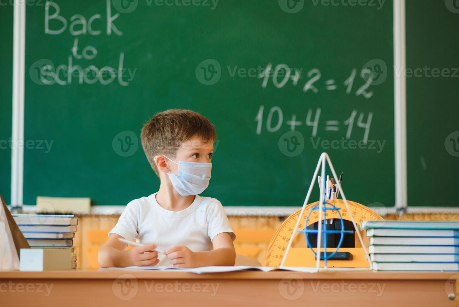 Little schoolboy wearing protective mask in classroom. Concept of epidemic photo