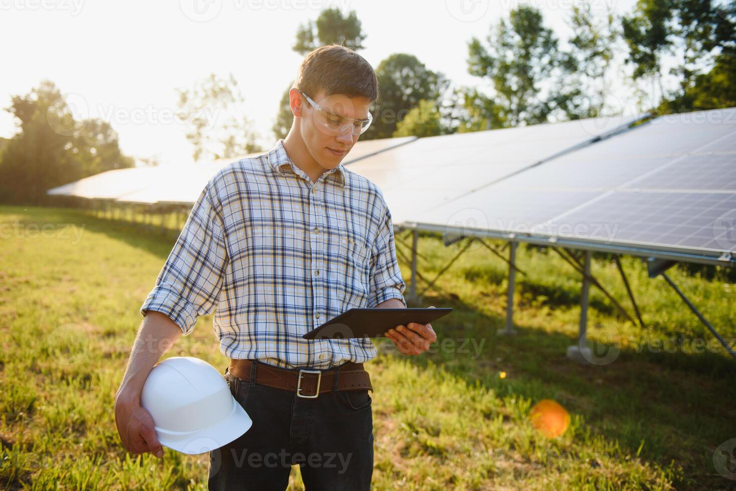 The portrait of a young engineer checks with tablet operation with sun, cleanliness on field of photovoltaic solar panels. Concept renewable energy, technology, electricity, service, green power. photo