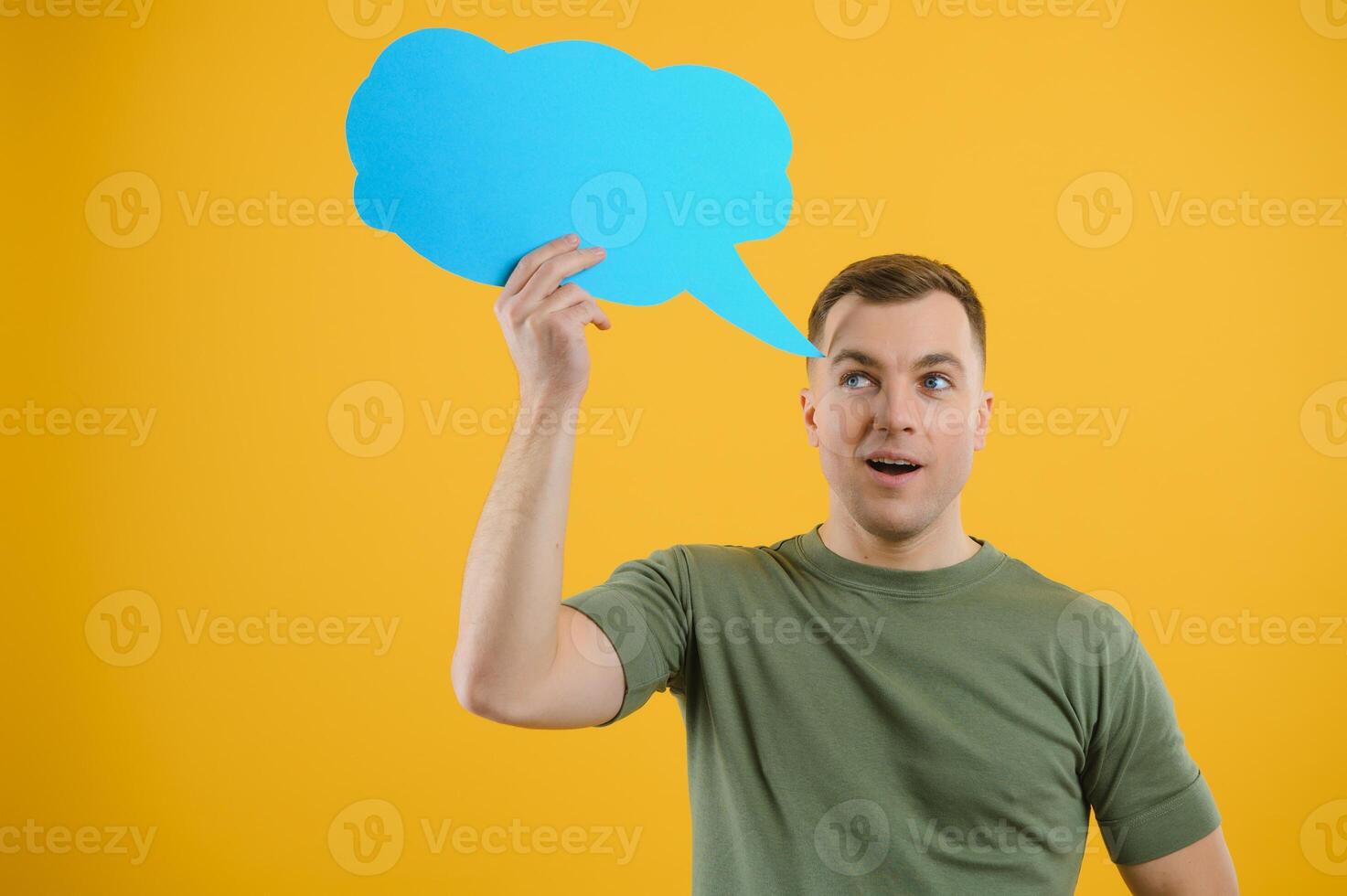 Cheerful young male pointing up and holding empty speech bubble with blank space for quote against vivid yellow background photo