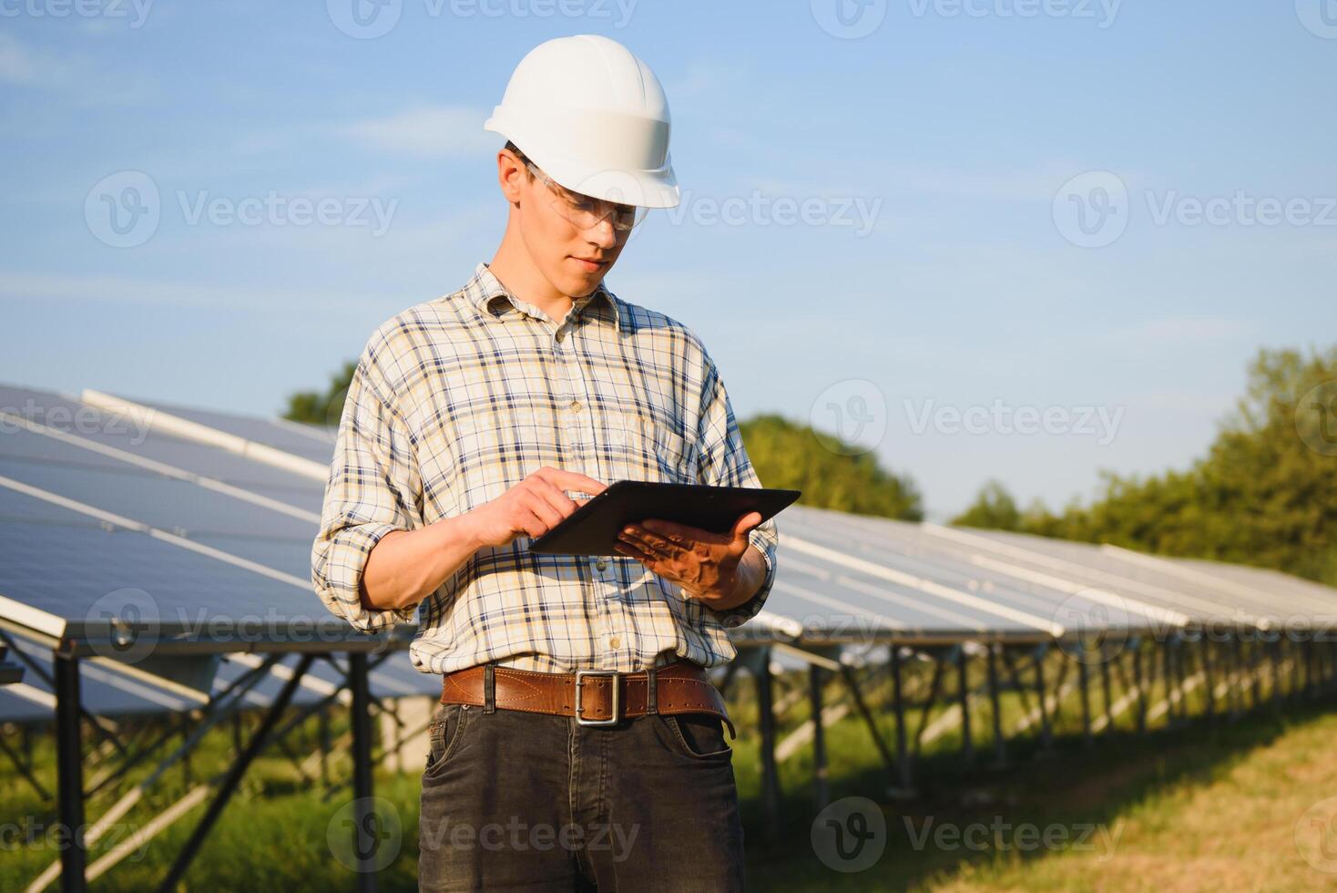 The portrait of a young engineer checks with tablet operation with sun, cleanliness on field of photovoltaic solar panels. Concept renewable energy, technology, electricity, service, green power. photo