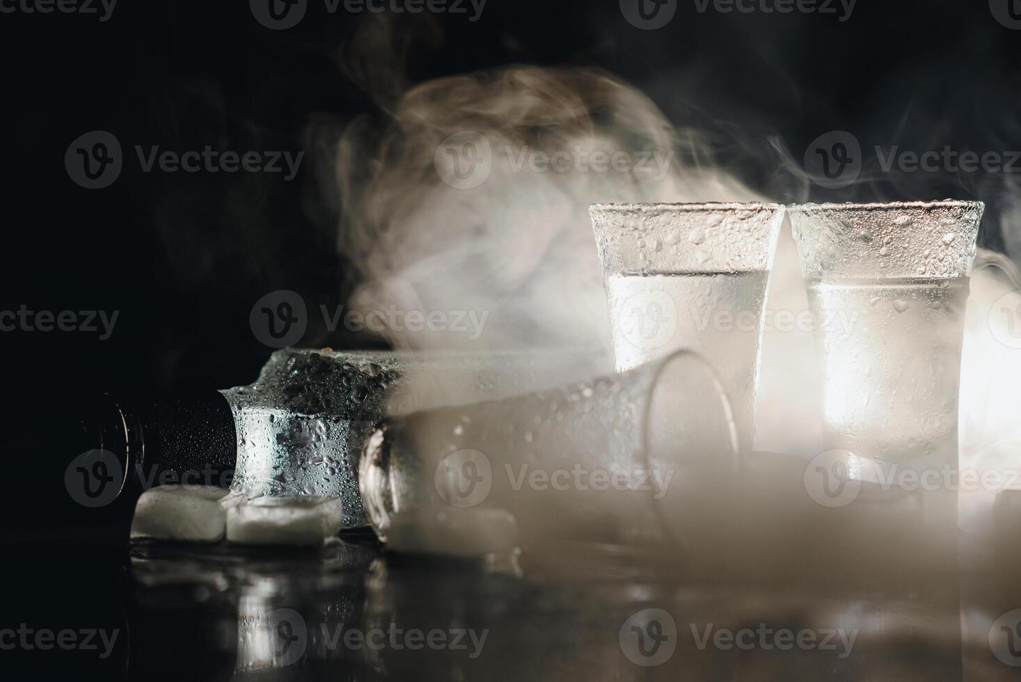 Close-up view of bottle of vodka with glasses standing on ice on black. photo