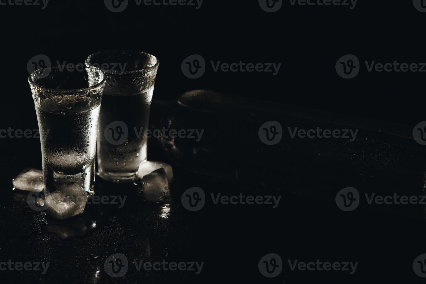 Vodka shots with ice on black table, copy space. photo
