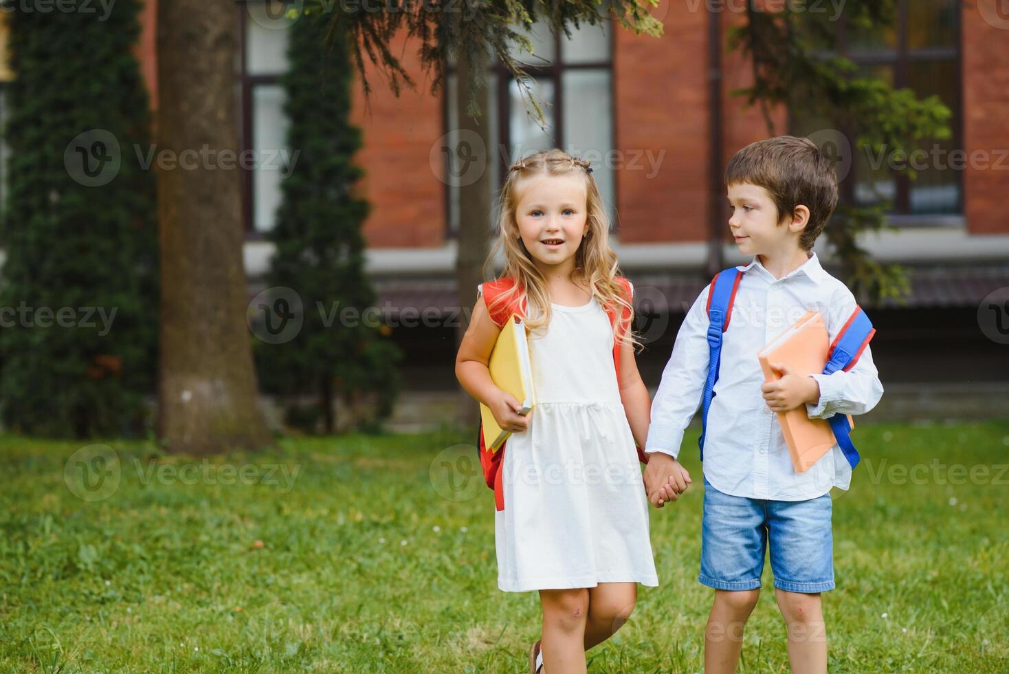 contento niños - chico y niña con libros y mochilas en el primero colegio día. emocionado a ser espalda a colegio después vacaciones. lleno longitud al aire libre retrato. foto