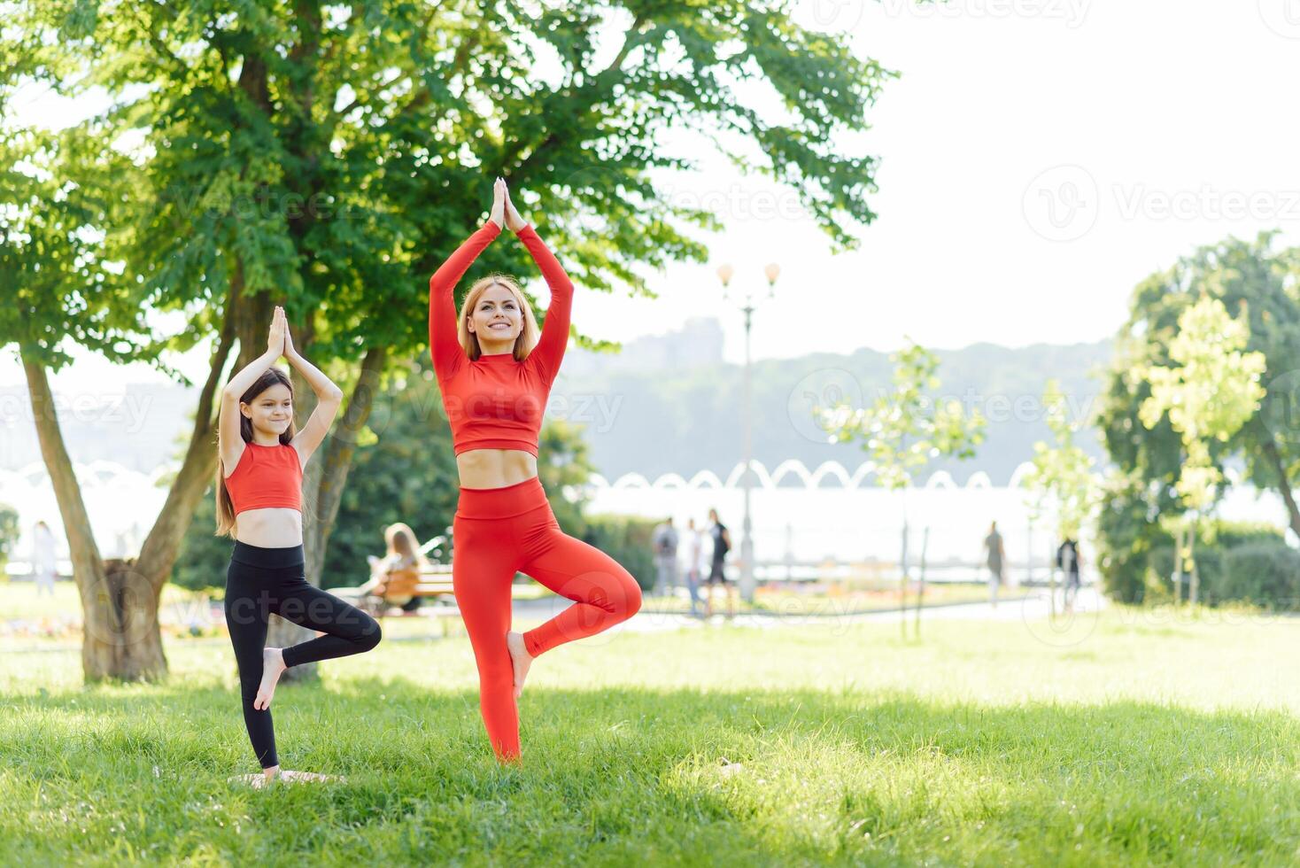 Mother and daughter doing yoga exercises on grass in the park at the day time. People having fun outdoors. Concept of friendly family and of summer vacation. photo