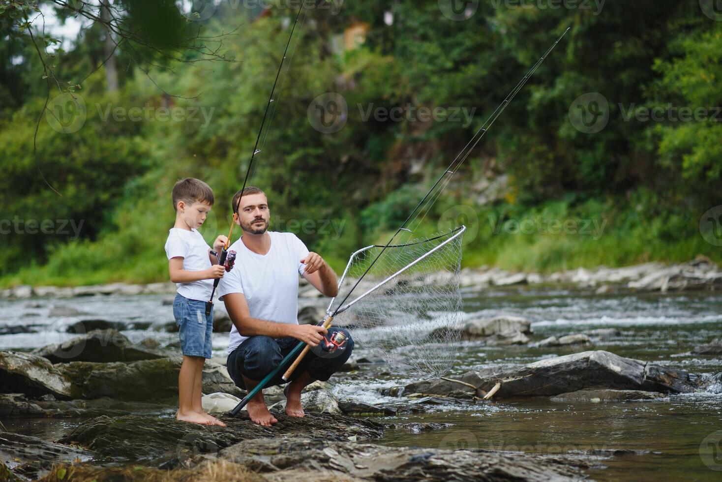 A father teaching his son how to fish on a river outside in summer sunshine. father's day. photo