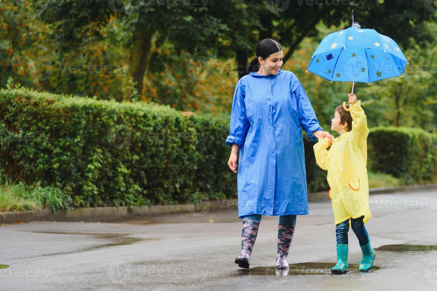 Mother with son walking in park in the rain wearing rubber boots photo