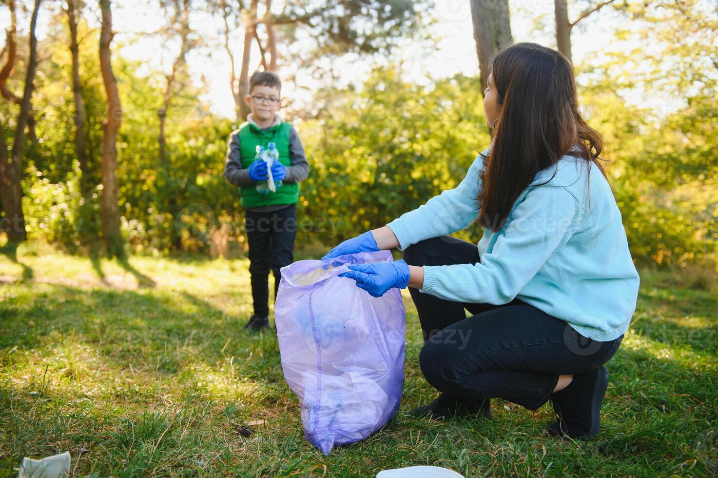 Mom teaches her son to clean up trash in nature. A woman removes plastic bottles in a bag. The topic of environmental pollution by garbage. photo