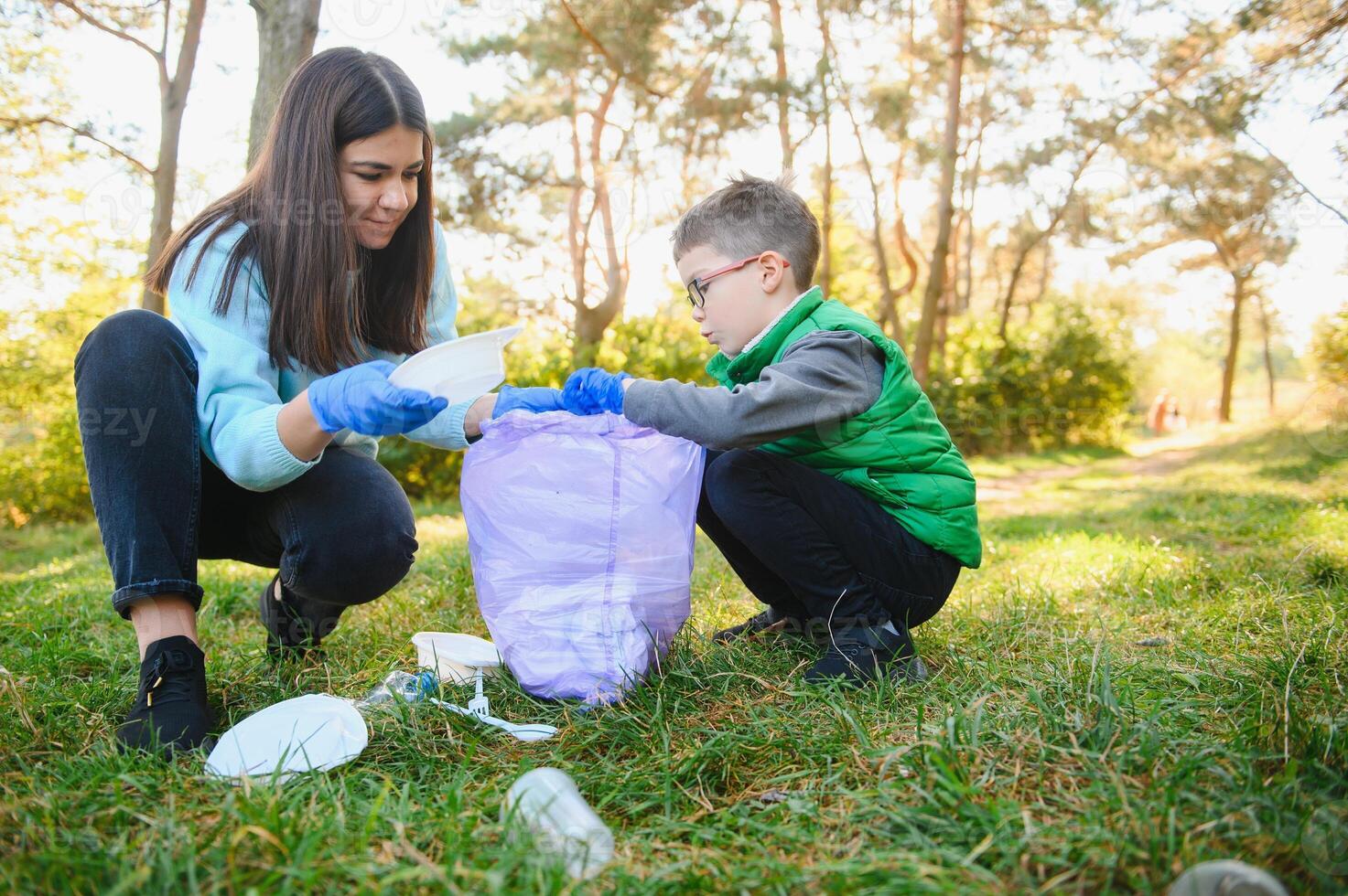 Mom teaches her son to clean up trash in nature. A woman removes plastic bottles in a bag. The topic of environmental pollution by garbage. photo