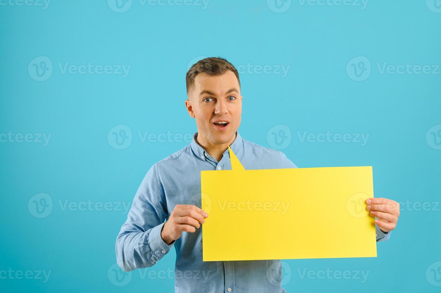 Joyful Caucasian man demonstrating blank placard on blue studio background, mockup for design photo