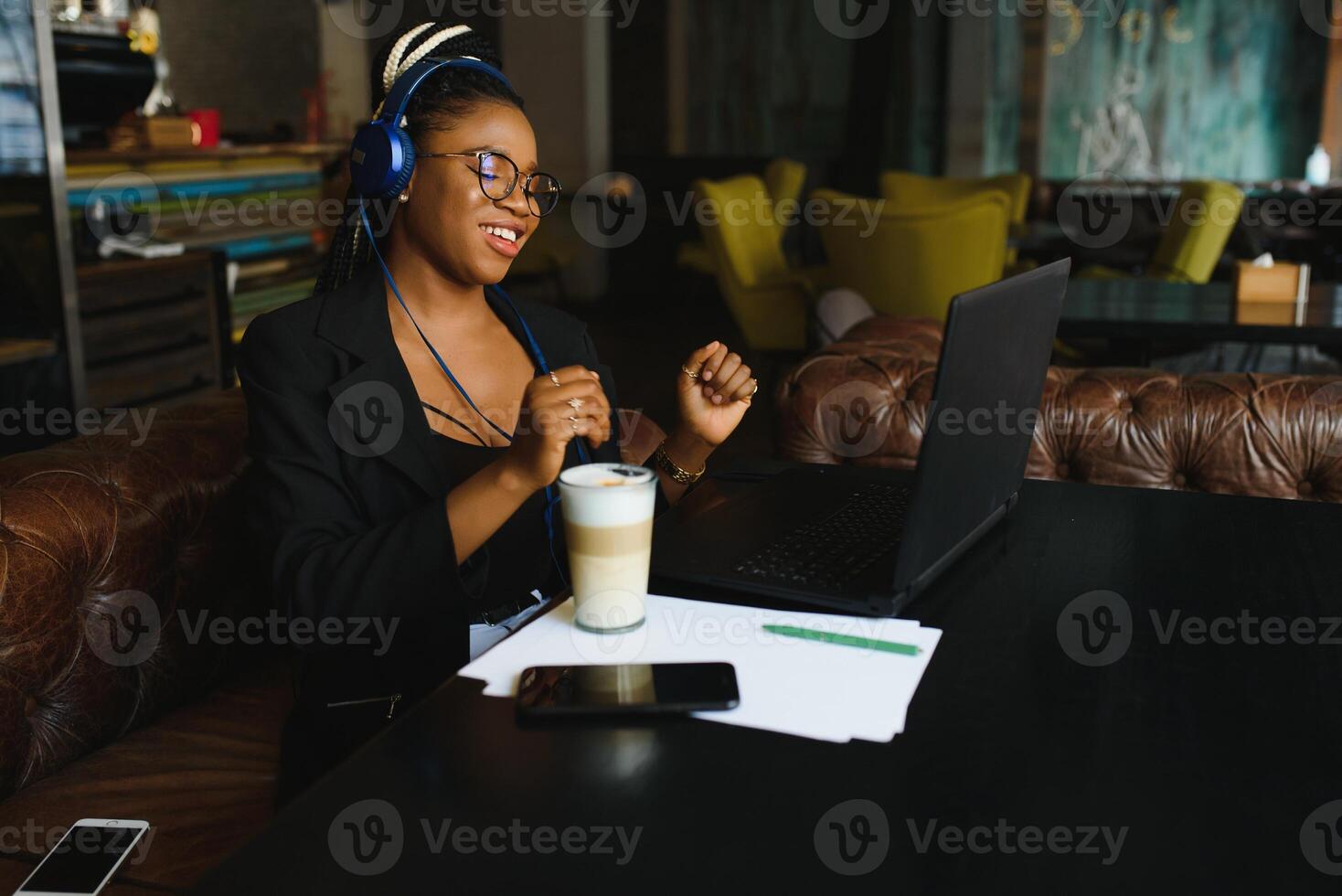 Attractive African American blogger with headphones and laptop communicating with followers in cafe photo